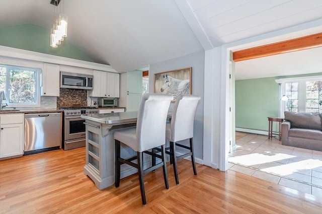 kitchen with stainless steel counters, hanging light fixtures, stainless steel appliances, a baseboard radiator, and white cabinets