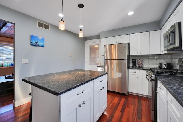 kitchen featuring tasteful backsplash, dark stone counters, stainless steel appliances, white cabinets, and dark hardwood / wood-style flooring