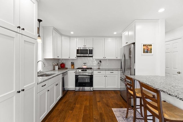 kitchen with dark wood-style flooring, stainless steel appliances, tasteful backsplash, white cabinets, and a sink