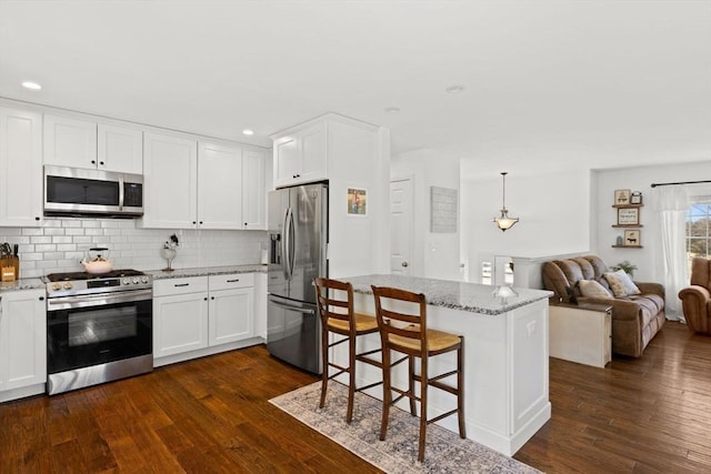 kitchen with tasteful backsplash, white cabinets, dark wood-style floors, light stone countertops, and stainless steel appliances