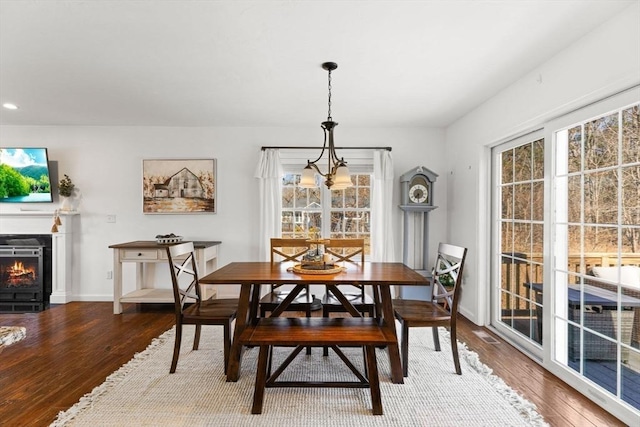 dining area featuring a warm lit fireplace, a chandelier, recessed lighting, wood finished floors, and baseboards