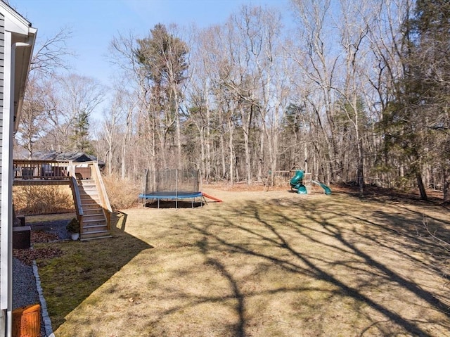 view of yard with a trampoline, a playground, a deck, and stairs