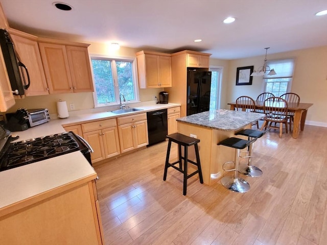 kitchen featuring black appliances, a breakfast bar, light brown cabinetry, a sink, and light wood finished floors