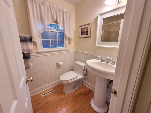 bathroom with wood finished floors, visible vents, a wainscoted wall, walk in shower, and toilet