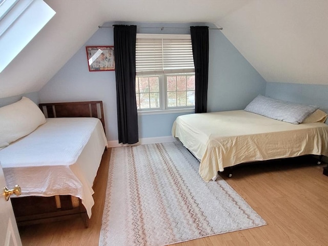 bedroom with lofted ceiling with skylight, baseboards, and wood finished floors