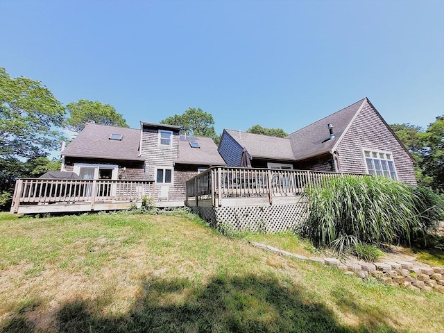 back of property with a deck, a lawn, and a shingled roof