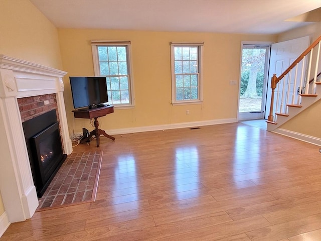 unfurnished living room featuring wood finished floors, stairway, a fireplace, and baseboards
