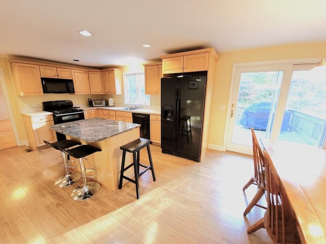 kitchen featuring light wood-style flooring, recessed lighting, black appliances, a kitchen bar, and a center island