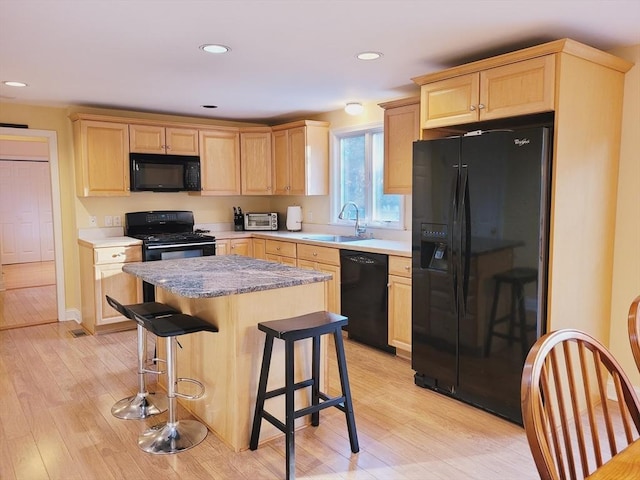kitchen featuring black appliances, light brown cabinets, light wood finished floors, and a sink
