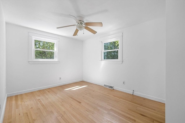 empty room featuring a wealth of natural light, light wood-type flooring, ceiling fan, and visible vents