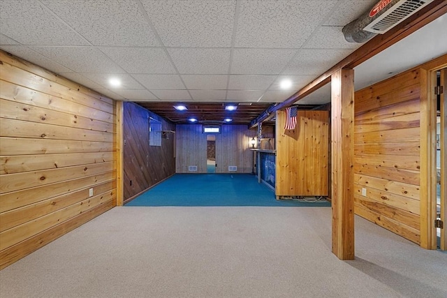 finished below grade area featuring wooden walls, carpet floors, a drop ceiling, and visible vents
