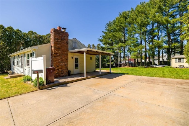 exterior space featuring a chimney, a carport, a yard, a patio, and concrete driveway