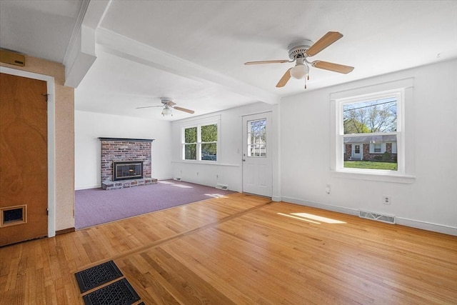 unfurnished living room with ceiling fan, visible vents, wood finished floors, and a fireplace