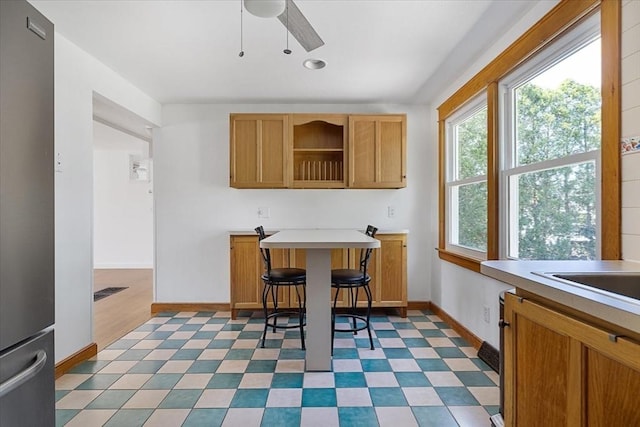 kitchen featuring light countertops, freestanding refrigerator, a ceiling fan, baseboards, and light floors