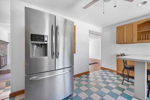 kitchen featuring baseboards, ceiling fan, a kitchen breakfast bar, light countertops, and stainless steel fridge with ice dispenser
