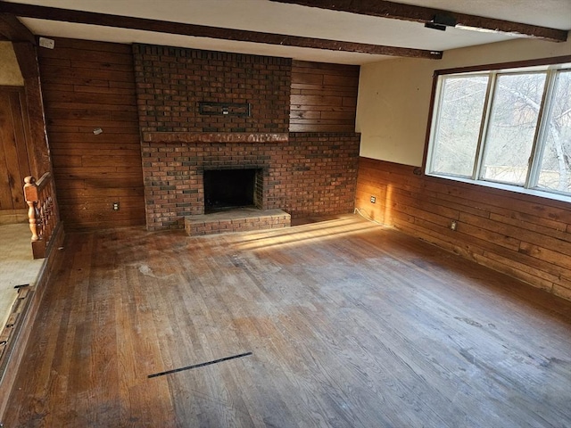 unfurnished living room featuring wood walls, a brick fireplace, beam ceiling, and wood finished floors