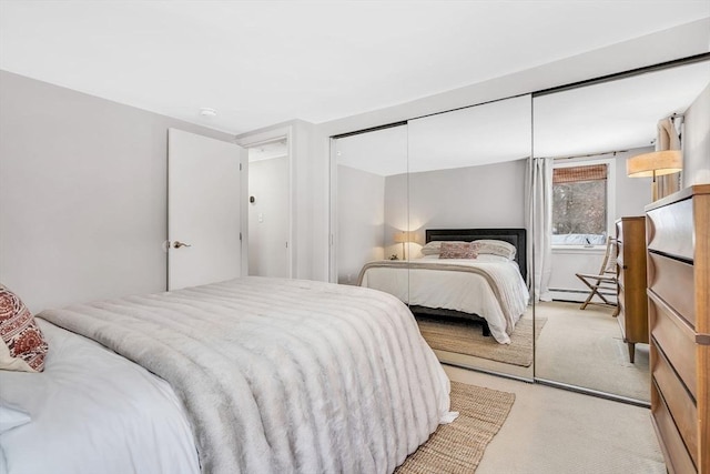 bedroom featuring a baseboard heating unit, a closet, and light colored carpet