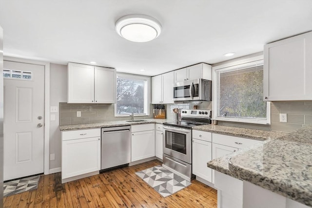 kitchen featuring stainless steel appliances, a sink, white cabinetry, light wood-type flooring, and light stone countertops