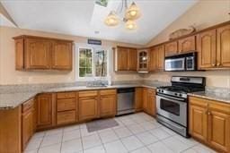 kitchen featuring brown cabinets, light tile patterned floors, stainless steel appliances, and lofted ceiling