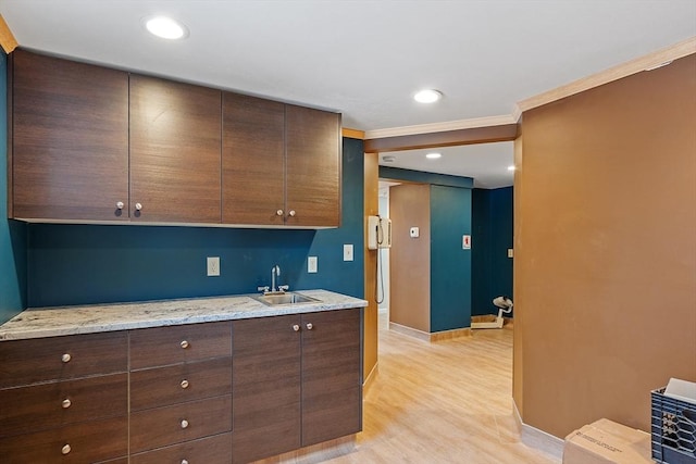 kitchen with light wood-style flooring, a sink, baseboards, dark brown cabinets, and crown molding