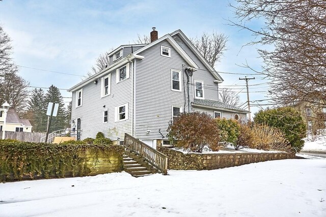 view of snow covered exterior with stairway and a chimney