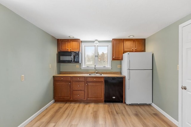 kitchen with light wood finished floors, brown cabinetry, a sink, black appliances, and baseboards