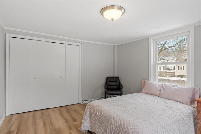 bedroom with light wood-type flooring, ornamental molding, and a closet