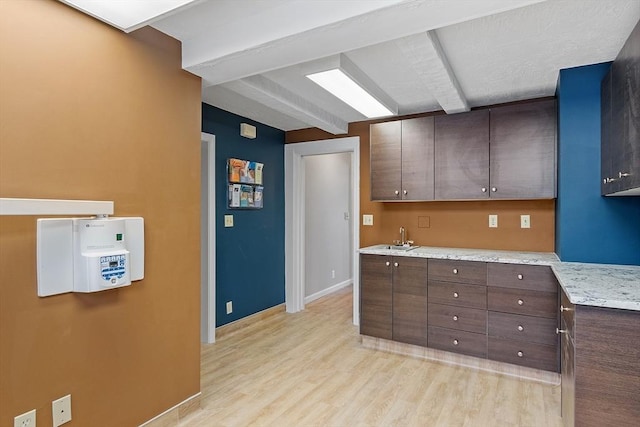 kitchen featuring baseboards, beam ceiling, dark brown cabinets, light wood-style floors, and a sink