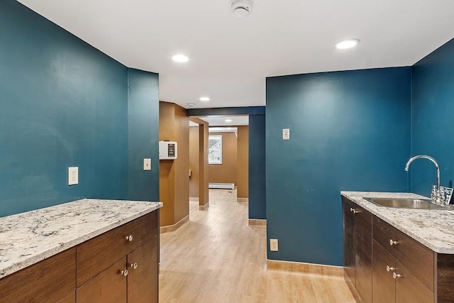 interior space with baseboards, light wood-style flooring, baseboard heating, a sink, and recessed lighting