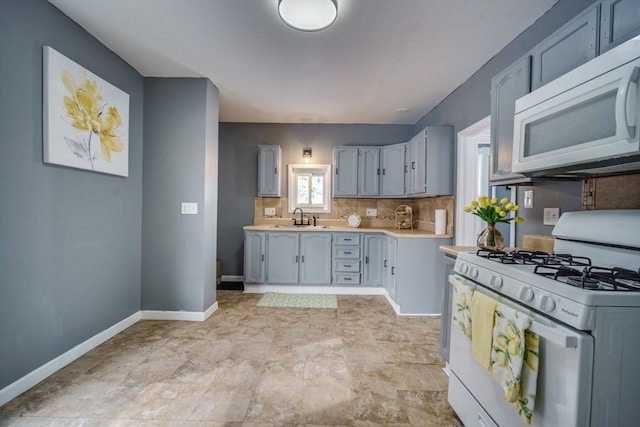 kitchen featuring light countertops, backsplash, a sink, white appliances, and baseboards