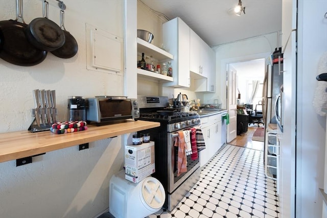 kitchen with gas range, white cabinets, open shelves, a sink, and butcher block counters
