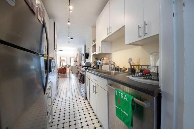 kitchen with stainless steel appliances, white cabinets, dark countertops, a sink, and track lighting
