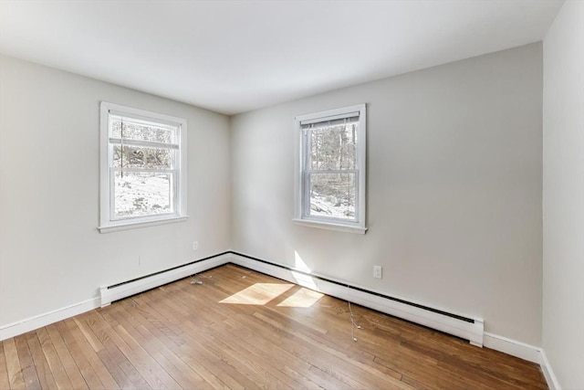 spare room featuring a baseboard heating unit, hardwood / wood-style floors, a wealth of natural light, and baseboards