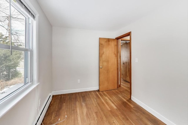 spare room with a baseboard heating unit, light wood finished floors, and baseboards