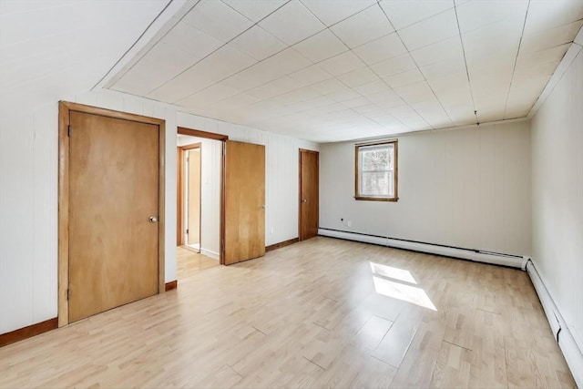 spare room featuring a baseboard heating unit, baseboard heating, baseboards, and light wood-style floors