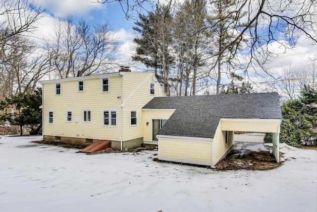 snow covered rear of property featuring a shingled roof and a chimney