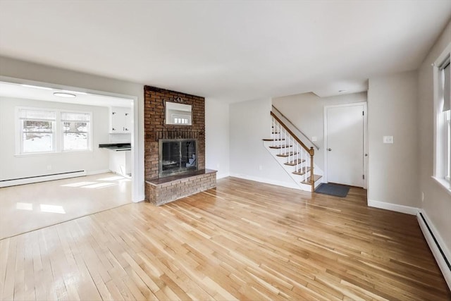 unfurnished living room featuring light wood-style floors, a brick fireplace, stairway, and baseboard heating