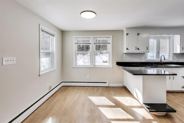 kitchen with dark countertops, white cabinets, baseboard heating, and decorative backsplash