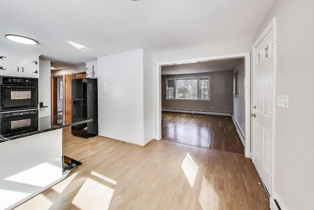 kitchen featuring white cabinets, light wood-style flooring, baseboard heating, black appliances, and a baseboard heating unit