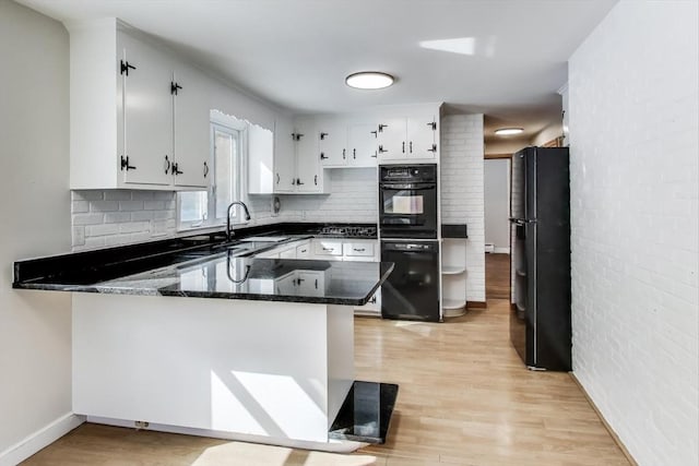 kitchen featuring backsplash, a sink, light wood-type flooring, a peninsula, and black appliances