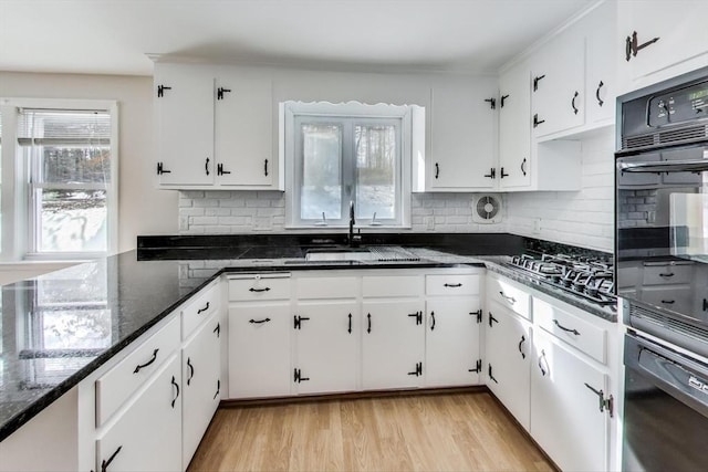 kitchen featuring light wood-style flooring, a sink, white cabinetry, tasteful backsplash, and dark stone countertops