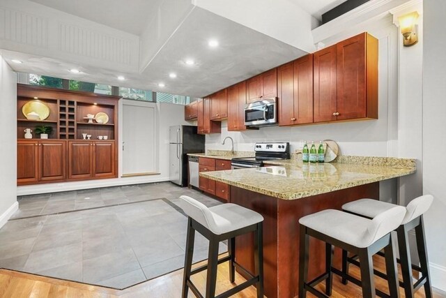 515 Franklin St Unit 4, Cambridge, MA 02139 - kitchen with appliances with stainless steel finishes, a peninsula, light stone countertops, a kitchen breakfast bar, and recessed lighting