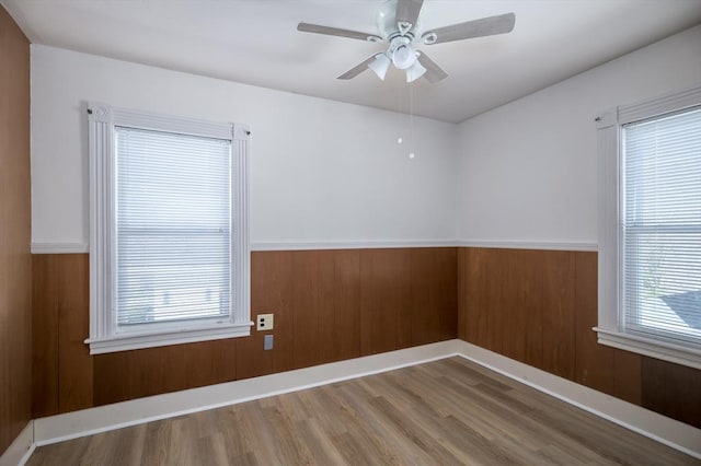 empty room featuring wooden walls, wood finished floors, a wainscoted wall, and ceiling fan