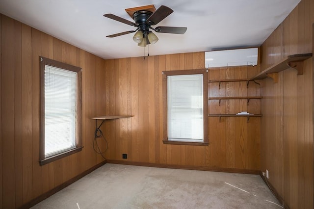 empty room featuring wooden walls, ceiling fan, baseboards, a wall unit AC, and light carpet