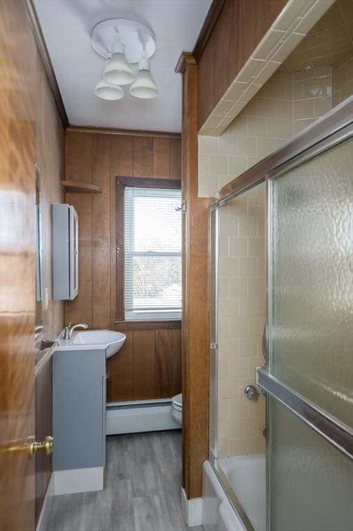 bathroom with vanity, wooden walls, wood finished floors, enclosed tub / shower combo, and baseboard heating