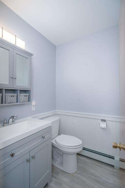 bathroom with vanity, wood finished floors, a wainscoted wall, a baseboard radiator, and toilet