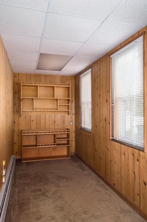 carpeted spare room featuring wooden walls, a baseboard heating unit, and a drop ceiling