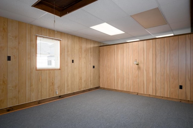 empty room featuring a drop ceiling, carpet, attic access, and wooden walls