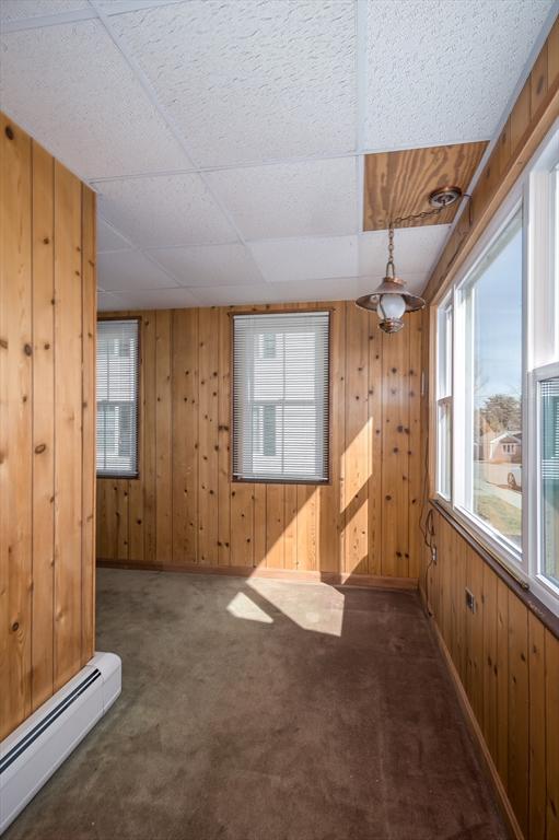 carpeted spare room with a baseboard heating unit, a paneled ceiling, and wood walls