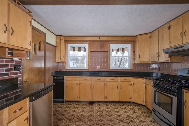 kitchen with under cabinet range hood, stainless steel appliances, dark countertops, and decorative backsplash